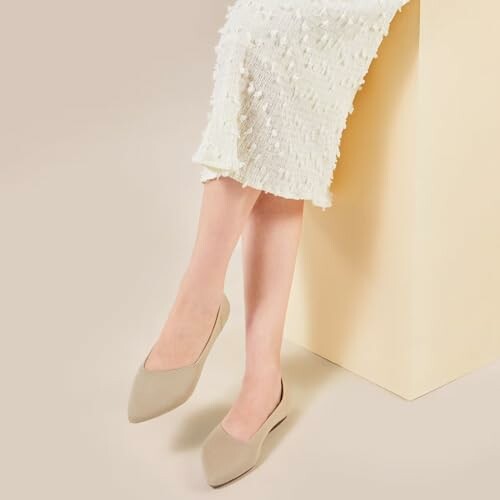 Woman wearing beige pointed flats with a white textured dress.