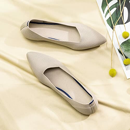 Pair of beige women's flat shoes on fabric with plant decor.