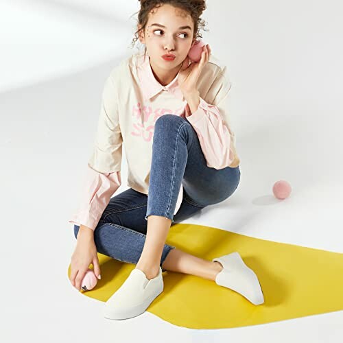 Person sitting on yellow mat wearing casual clothes and white sneakers.