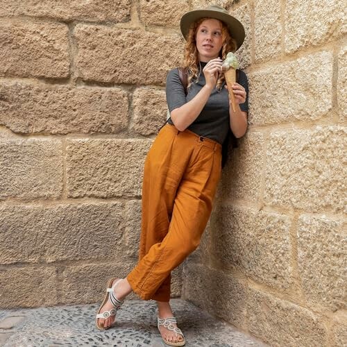 Woman in orange pants and hat eating ice cream against stone wall