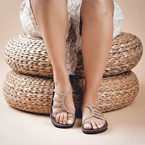 Woman sitting on woven ottomans wearing sandals.